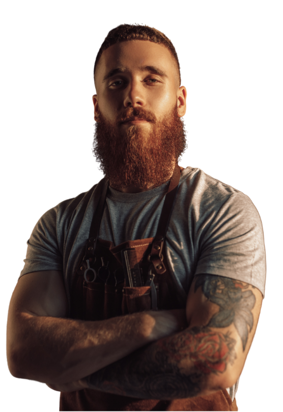 A ginger beard male barber with hand tattoos crossing his hands.